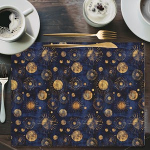 May include: A blue and gold placemat with a repeating pattern of suns and moons. The placemat is made of a textured fabric and has a subtle distressed look.