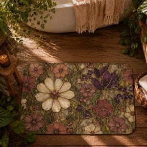May include: A rectangular bath mat featuring a stained glass style floral pattern with a large central white flower surrounded by smaller purple, pink, and cream blossoms, green leaves, and dark outlines on a textured, multi-coloured background.