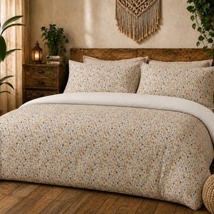 May include: A bedding set featuring a duvet cover and two matching pillowcases with a small-scale floral pattern in shades of yellow, blue, and green on a cream background, paired with a solid white flat sheet folded over the top edge.