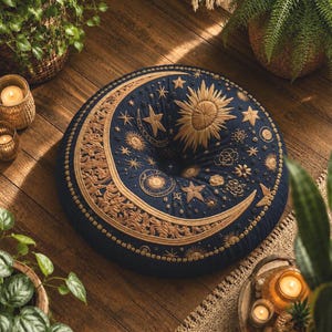 May include: A round, dark blue floor cushion featuring intricate gold-colored embroidery of a large crescent moon, a radiant sun, and various stars. The central design includes a tufted button detail, with decorative patterns along the border.
