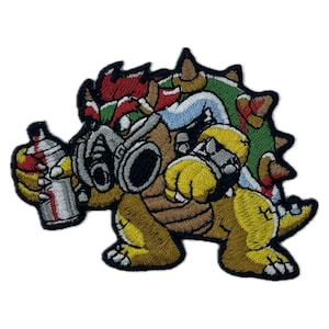 May include: An embroidered patch featuring a cartoon character resembling a turtle wearing a gas mask and holding a spray paint can. The character is yellow, brown, green, red, and blue.