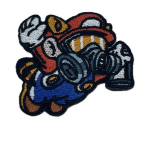 May include: Embroidered patch featuring a cartoon character wearing a gas mask. The character is red, blue, and yellow with black outlines. The gas mask is grey and black.
