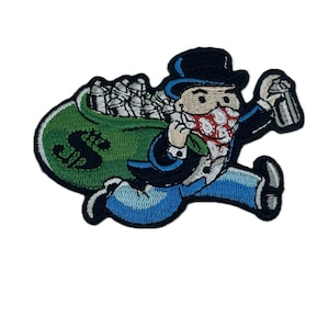 Peut inclure: Un patch brodé représentant un personnage de dessin animé courant avec un sac d'argent. Le personnage porte un chapeau haut de forme noir, un bandana rouge à pois blancs, une chemise bleue et un pantalon bleu. Le sac est vert et porte un signe dollar.