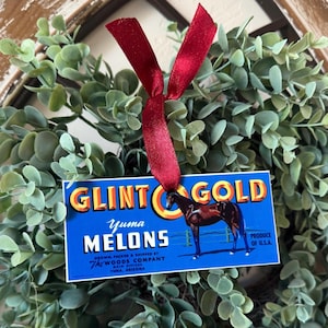 May include: A blue and yellow vintage-style Christmas ornament with a horse and the text "Glintgold Yuma Melons Grown, Packed & Shipped by The Woods Company Main Offices Yuma, Arizona Produce of U.S.A."