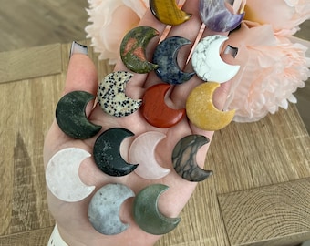 May include: A collection of 12 crescent moon shaped polished stones in various colors and patterns, including green, red, white, yellow, and brown.