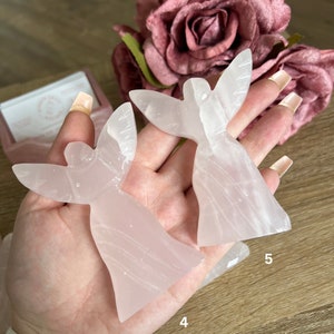 Puede incluir: Dos figuritas de &aacute;ngel rosas talladas en cristal de selenita. Las figuritas miden aproximadamente 10 cm de alto y tienen una apariencia delicada y transl&uacute;cida.