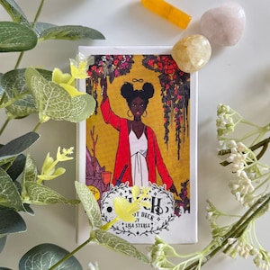 Puede incluir: Una caja de baraja de tarot con una ilustración de una mujer con una chaqueta roja, con el texto "Witch Tarot Deck by Lisa Sterle". La imagen incluye un cristal amarillo, una piedra rosa y una piedra amarilla. Decoraciones florales verdes y blancas rodean la baraja.