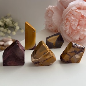 May include: Five polished stone carvings in various shapes and sizes. One is a tall, slender mustard yellow piece. The others are shorter, angular forms in shades of deep burgundy, tan, and brown with visible natural veining and smooth surfaces.