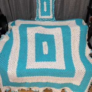 May include: A crocheted throw blanket in turquoise and white with a square pattern. The blanket has a crocheted border and a matching pillow.