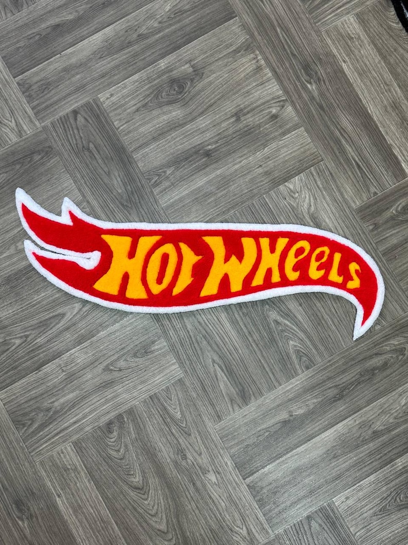 May include: A red and yellow Hot Wheels logo with a white outline. The logo is shaped like a flame and has a white border.