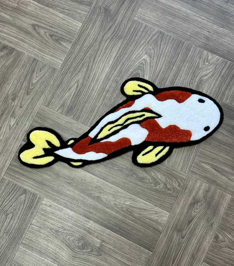 May include: A red, white, and yellow plush rug shaped like a koi fish. The rug has a black outline and is made of soft, fuzzy material.