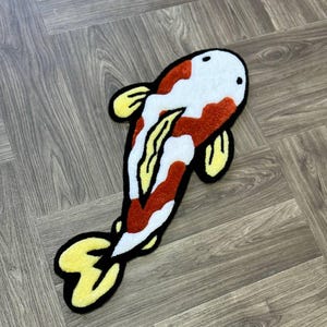 May include: A white and red koi fish rug with yellow fins and black outlines. The rug is made of a soft, plush material and is perfect for adding a touch of whimsy to any room.
