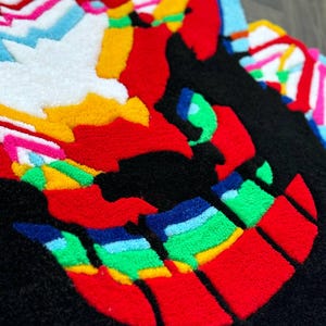 May include: A tufted rug featuring a stylized, multi-colored graphic design. The composition includes bold sections of black, vibrant red, bright yellow, white, light blue, and green yarn, creating a textured, high-contrast abstract pattern.