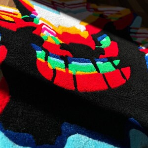May include: A tufted rug featuring a stylized, multi-colored graphic design with a prominent black background. The pattern includes vibrant red, green, yellow, blue, and white sections with a textured, plush surface and irregular, jagged edges.