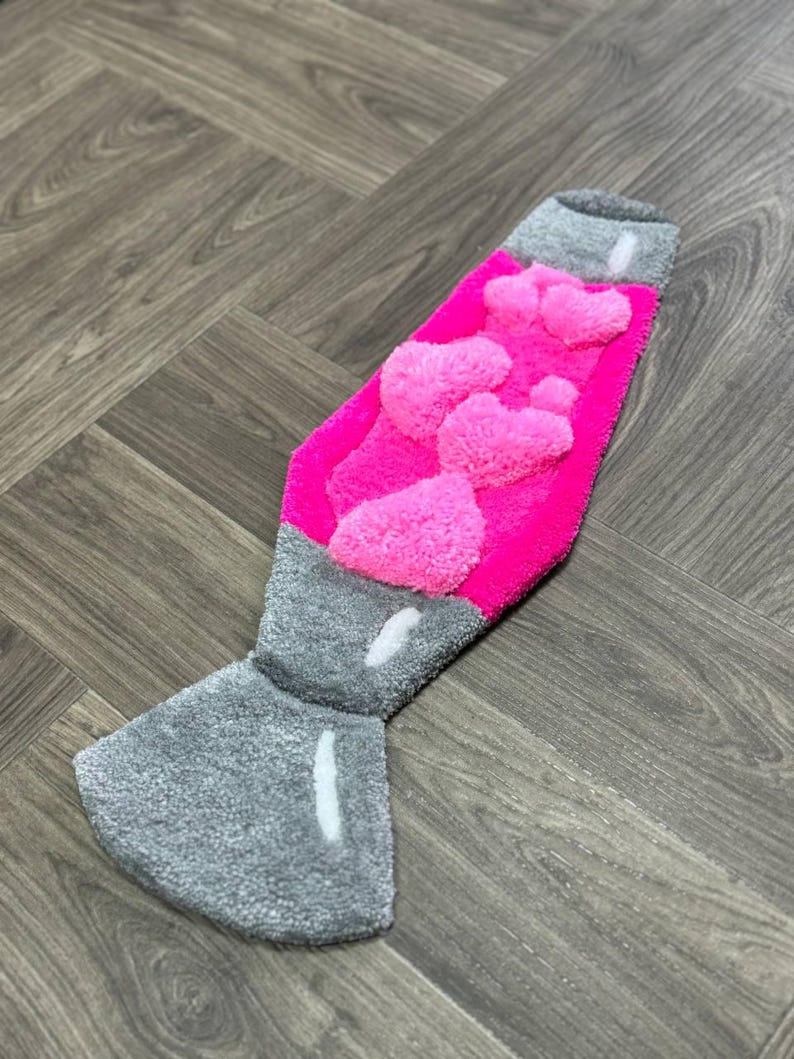 May include: A pink and gray rug shaped like a lava lamp. The lamp has a pink, fuzzy texture and a gray base.