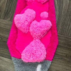May include: A pink and gray rug with a design of hearts made of fluffy yarn.
