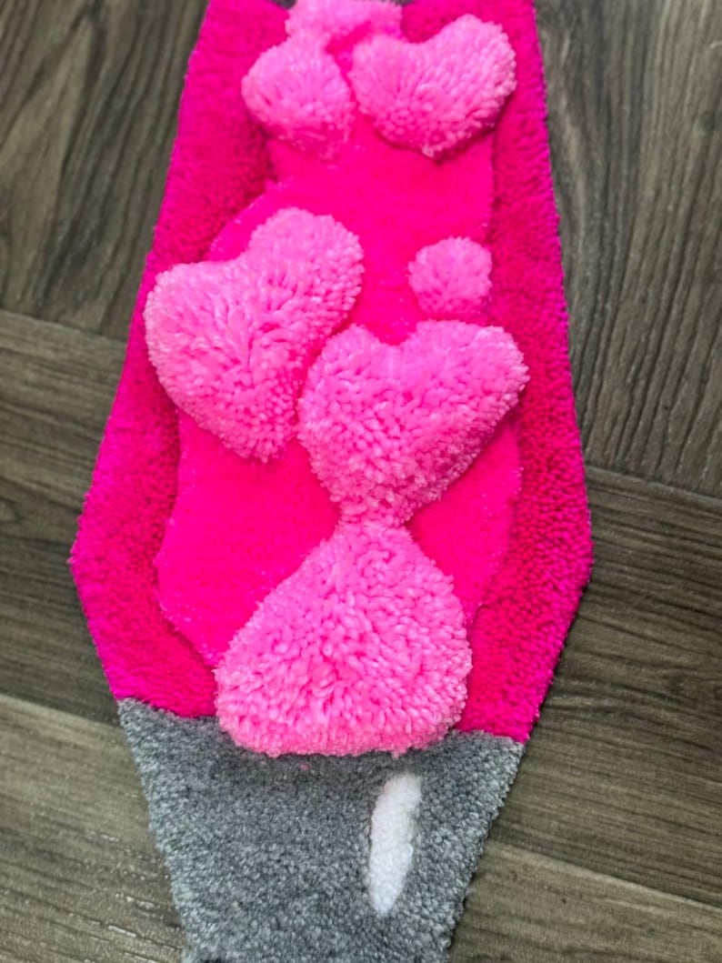 May include: A pink and gray rug with a design of hearts made of fluffy yarn.