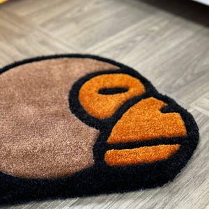 May include: A brown, black, and orange rug with a stylized monkey face design.