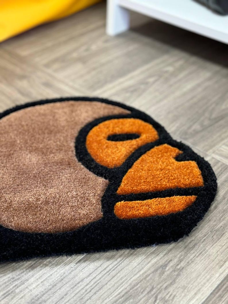 May include: A brown, black, and orange rug with a stylized monkey face design.