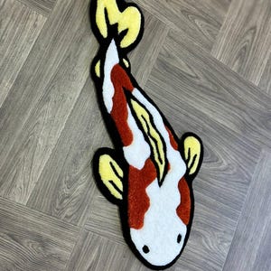May include: A white and red koi fish rug with yellow fins and black outlines. The rug is made of fluffy, textured material and is perfect for adding a touch of whimsy to any room.
