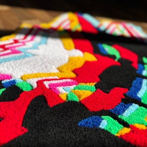 May include: A tufted textile piece featuring a high-contrast design with a black background and vibrant, raised yarn sections in red, white, yellow, bright pink, light blue, and green, creating a textured, multi-colored abstract pattern.