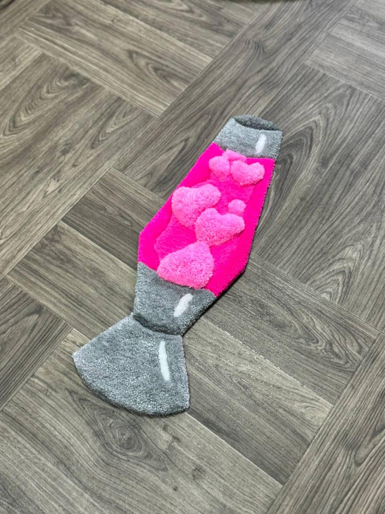 May include: A pink and gray lava lamp rug with a fuzzy texture. The lamp is shaped like a traditional lava lamp with a round base and a tall, thin neck.