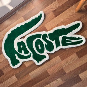 May include: A white and green rug with the word "LA COSTE" in green letters. The rug is shaped like an alligator.