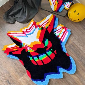 May include: A tufted rug featuring a stylized, abstract graphic design with a vibrant color palette of black, red, white, yellow, and blue. The rug has an irregular, jagged shape with layered, glitch-like patterns and a textured surface.