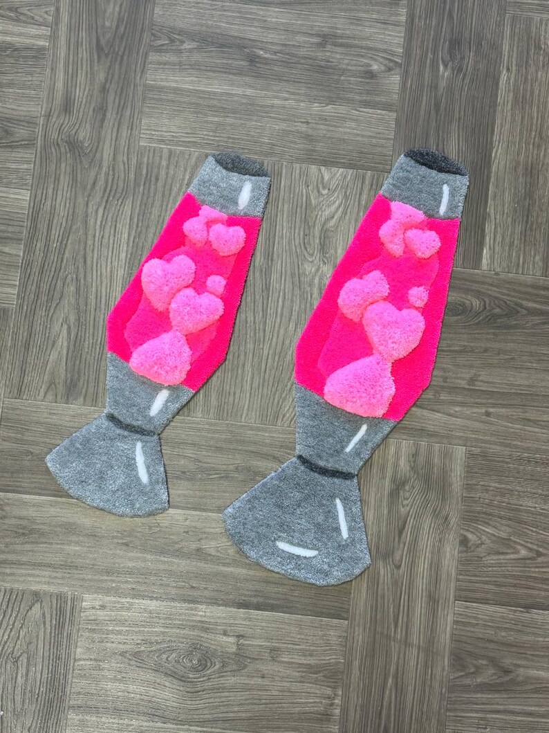 May include: Two gray and pink lava lamp shaped rugs with pink hearts in the center. The rugs are on a wood floor.