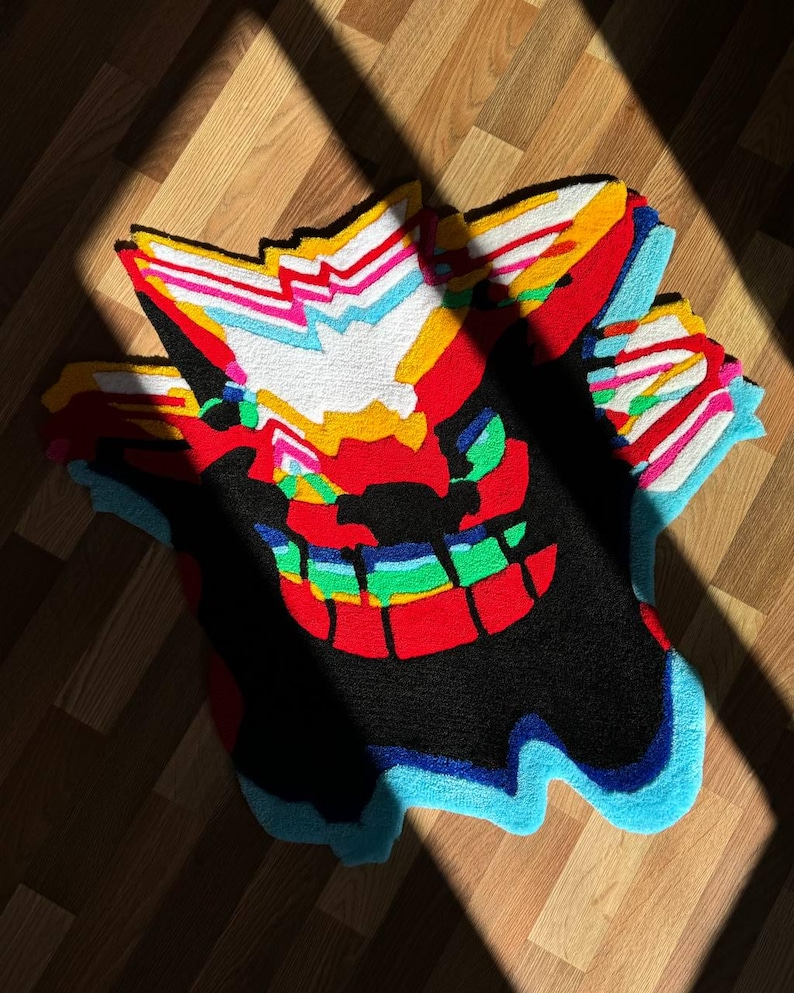 May include: A tufted rug featuring a stylized, multi-layered graphic design with vibrant colors including red, black, white, yellow, light blue, and green. The rug has an irregular, jagged shape with overlapping patterns that create a visual depth effect.