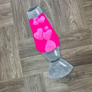 May include: A pink and gray lava lamp rug with a fuzzy texture and a heart design.