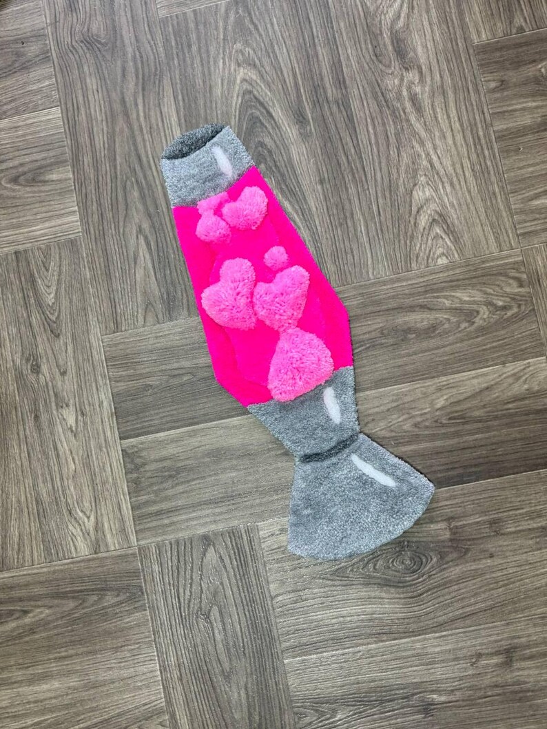 May include: A pink and gray lava lamp rug with a fuzzy texture and a heart design.
