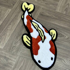 May include: A white and orange koi fish rug with yellow fins. The rug is made of a soft, plush material and has a black outline.