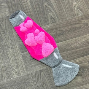 Könnte beinhalten: Ein rosa und grauer Teppich in Form einer Lava-Lampe mit einer flauschigen Textur. Die Lampe hat eine rosa Basis mit weißen und rosa flauschigen Herzen im Inneren.
