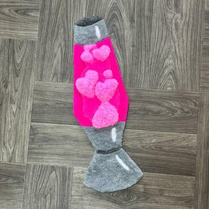 May include: A pink and gray lava lamp rug with a fuzzy texture. The lamp is filled with pink hearts.