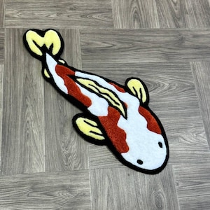 May include: A white and orange koi fish rug with yellow fins. The rug is made of a soft, plush material and has a cartoon-like design.