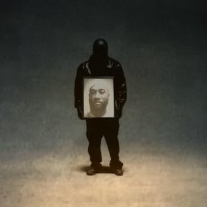 May include: A person wearing a black jacket holds a framed photo of a man with a beard. The photo is in black and white.
