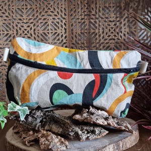 Puede incluir: Una bolsa blanca con cremallera con un patrón abstracto colorido que presenta círculos y remolinos negros, rojos, amarillos, azules y verdes.