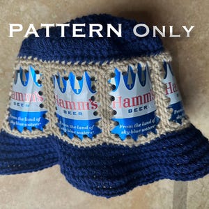 May include: A dark blue crocheted bucket hat featuring a band of beige yarn connecting four Hamm's beer can aluminum segments. The text PATTERN ONLY is printed in white across the top of the hat, which displays the Hamm's beer logo.