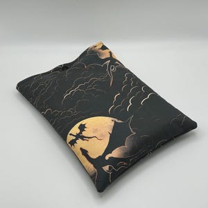 May include: A rectangular black cushion with a fantasy-themed print. The design includes dragons, a full moon, and clouds in gold and tan hues. The artwork is set against a dark backdrop, creating a striking contrast.