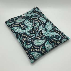 May include: A rectangular fabric pouch featuring a dark navy blue background with a repeating pattern of light teal dragons, crescent moons, paisley shapes, and small floral sprigs. The pouch is secured at the top center with a single white snap button.