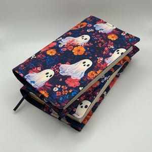 May include: Two stacked book covers with a dark blue floral pattern and white ghost illustrations. The covers have a black ribbon bookmark. The floral design includes orange, red, and yellow flowers.