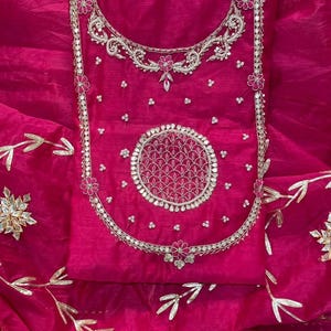 May include: A vibrant fuchsia-colored garment with intricate silver embroidery. The design features floral and circular patterns, with delicate gold leaf accents. The fabric has a sheer, flowing quality, suggesting a formal or festive attire.