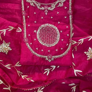 May include: A vibrant fuchsia-colored garment with intricate silver embroidery. The design features floral and circular patterns, with delicate gold leaf accents. The fabric has a sheer, flowing quality, suggesting a formal or festive attire.