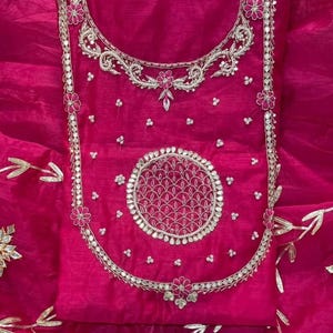 May include: A vibrant fuchsia-colored garment with intricate silver embroidery. The design features floral and geometric patterns, including a large circular motif. The fabric has a sheer, flowing quality, suggesting a formal or festive attire.