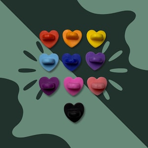 May include: A selection of ten heart-shaped enamel pins in a range of colours: red, orange, yellow, light blue, dark blue, purple, dark purple, pink, peach, and black. Each pin has a matching coloured post and clasp.