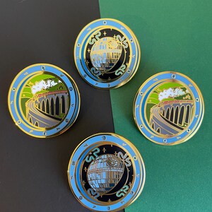 May include: Four round enamel pins with gold trim. Two pins feature a train on a bridge, and two feature a Death Star design. The pins have blue, black, green, and gold accents. The background is black and green.