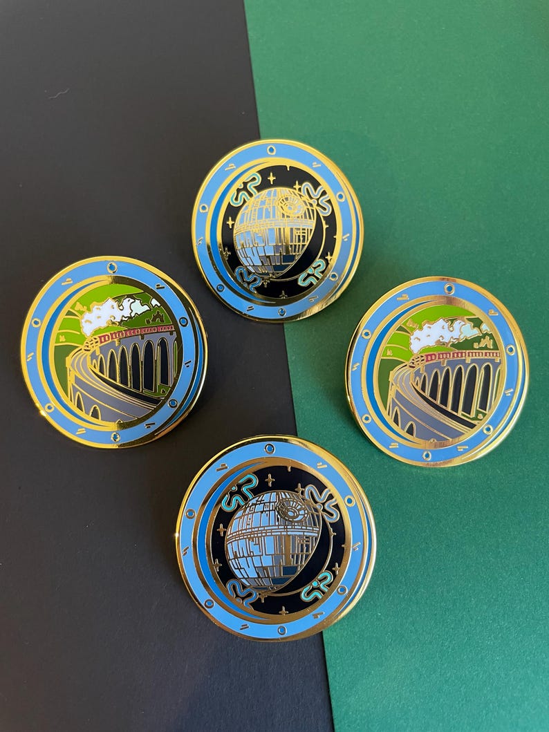 May include: Four round enamel pins with gold trim. Two pins feature a train on a bridge, and two feature a Death Star design. The pins have blue, black, green, and gold accents. The background is black and green.