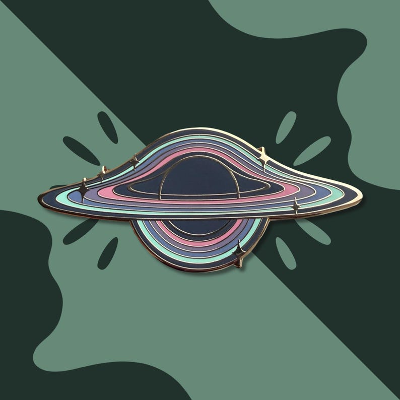 May include: A black hole enamel pin with a gold border. The pin features a dark blue center with concentric rings in shades of pink, blue, and teal. Small star-shaped accents are placed around the outer edge. The background is a dark green with a leaf-like pattern.