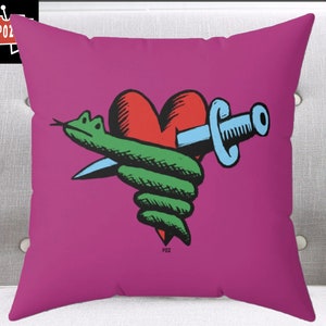 Puede incluir: Una almohada rosa con una serpiente verde envuelta alrededor de un corazón rojo con una daga azul que lo atraviesa. La imagen tiene el texto "POZ" en la parte inferior.